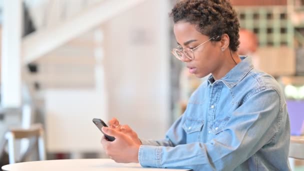 Mulher Africana comemorando o sucesso no Smartphone no Cafe — Vídeo de Stock