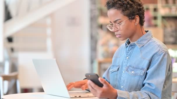 Mujer africana trabajadora usando Smartphone y Laptop en Café — Vídeos de Stock