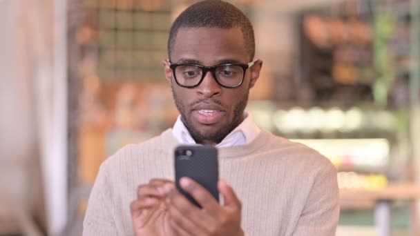 Akıllı telefonda başarıyı kutlayan heyecanlı Afrikalı adamın portresi — Stok video