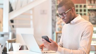 Kafede akıllı telefon ve dizüstü bilgisayar kullanan Afrikalı adam.