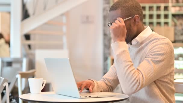 Uomo africano stressato con il computer portatile che ha mal di testa in Cafe — Video Stock