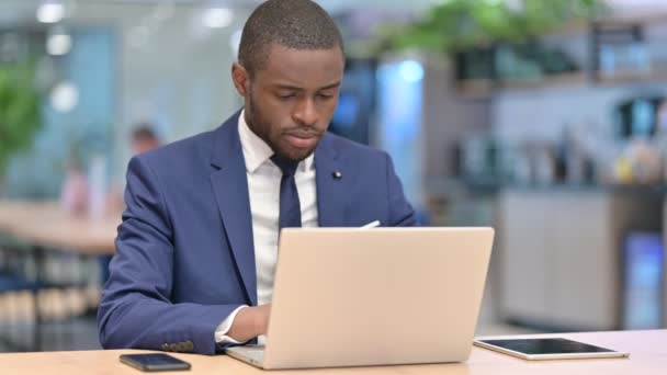 Африканський бізнесмен з ноутбуком, який дивиться на камеру в кафе — стокове відео