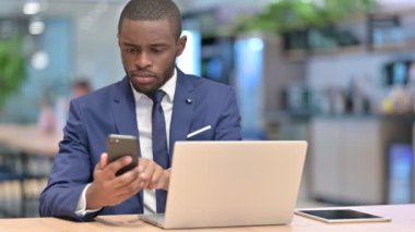 Ofiste akıllı telefon ve dizüstü bilgisayar kullanan çalışkan Afrikalı iş adamı 