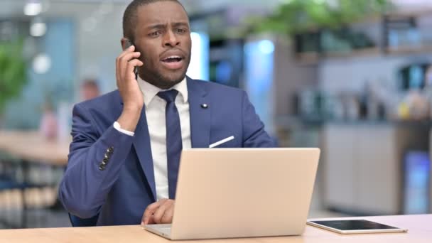 Empresário Africano com Laptop Talking no Smartphone no Escritório — Vídeo de Stock