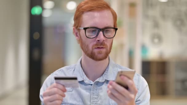 Портрет рыжеволосого человека с успехом онлайн-платежей на смартфоне — стоковое видео