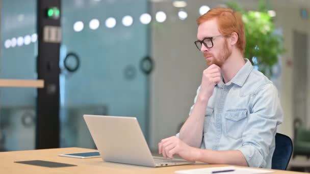 Ofisteki laptopta düşünen ve çalışan dalgın kızıl saçlı adam. — Stok video