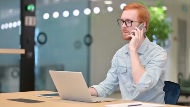 Casual rousse homme avec ordinateur portable parler sur Smartphone au bureau — Video