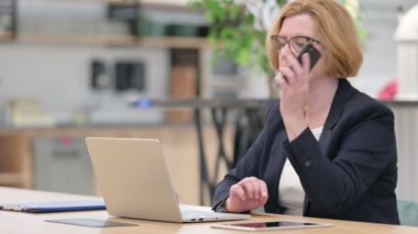 Dizüstü bilgisayarlı yaşlı iş kadını Ofiste Smartphone ile konuşuyor 