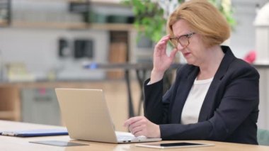 Dizüstü bilgisayarlı yaşlı iş kadını ofiste baş ağrısı çekiyor. 