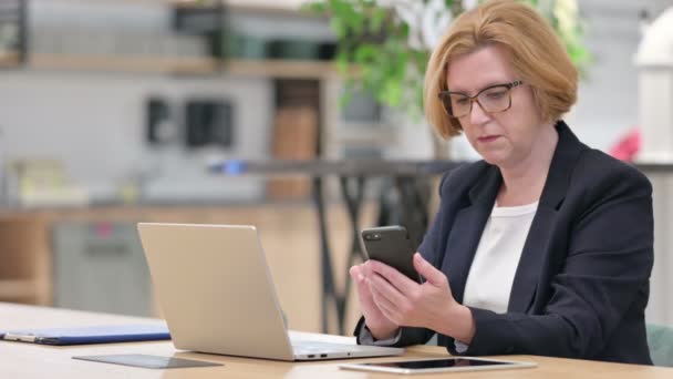 Стара бізнес-леді працює на ноутбуці та смартфоні в офісі — стокове відео