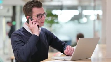 Dizüstü bilgisayarlı genç iş adamı Smartphone 'da konuşuyor 