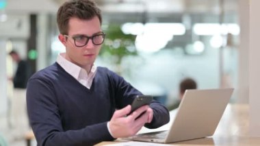 Akıllı telefon ve dizüstü bilgisayar kullanan genç bir iş adamı 