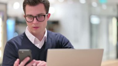 Dizüstü bilgisayarlı genç iş adamı Smartphone 'da konuşuyor 