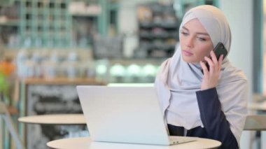 Dizüstü bilgisayarlı genç Arap Kadın Akıllı Telefonla Konuşuyor 