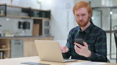 Kızıl Sakallı Adam akıllı telefon ve dizüstü bilgisayar üzerinde çalışıyor. 