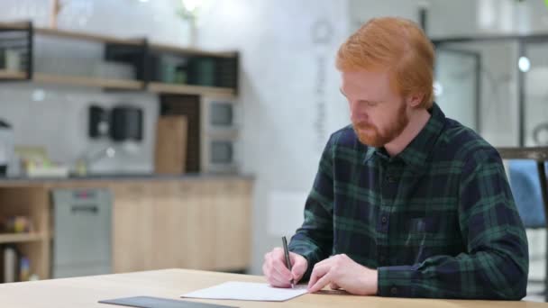 若いひげの赤毛の男がカフェで紙に書く — ストック動画