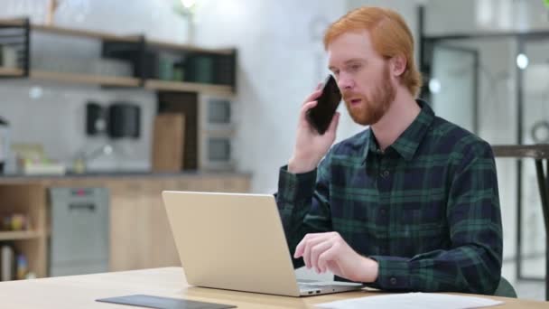Barba rossa uomo con computer portatile parlare su Smartphone — Video Stock