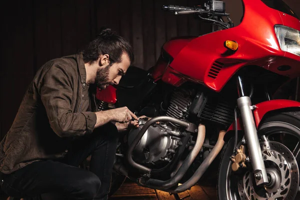 Bir adam bir motosikleti tamir ediyor. Garajdaki genç adam.