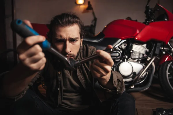 Молодой Человек Гараже Среди Мотоцикла Держит Руках Инструмент Смотрит Человек — стоковое фото