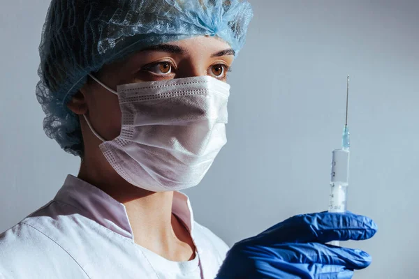 Girl doctor looks at a syringe with medicine. Masked doctor