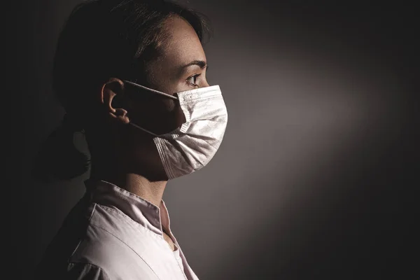 A female doctor in a mask is looking forward. Close-up side photo