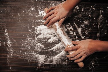 Tahta bir masanın üzerinde yuvarlanan iğne ve un. Ellerini merdaneye koy. Yakın plan fotoğraf.