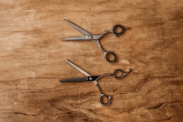 Two hairdressing scissors lie on a wooden table parallel to each other.
