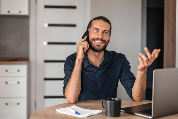 A young man is talking on the phone and smiling. A man works at home