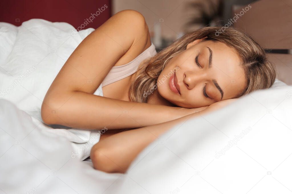 Mixed race young woman sleeping in a white bed.
