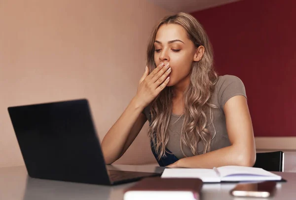 Mixed race young woman yawns and works on a laptop at home. Tired young girl. Work at home. Remote work