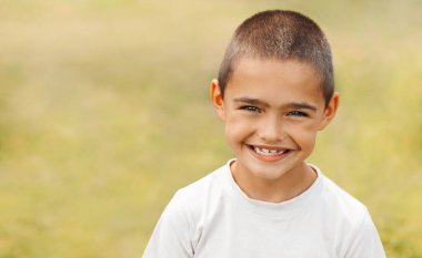 Sokakta gülümseyen bir çocuğun portresi, yeşil çimenlerin arka planında, yakın plan