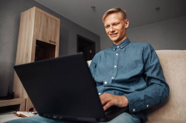 Neşeli genç adam evdeki kanepede otururken bilgisayarına bir mesaj yazıyor.