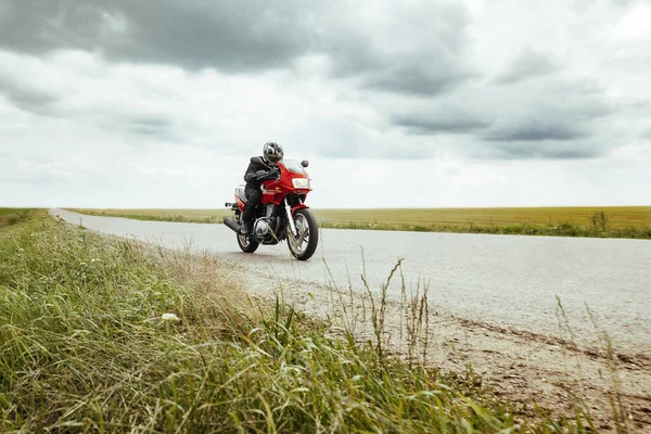 Bisikletli, tarlanın yakınındaki bir kır yolunda motosiklet sürüyor.
