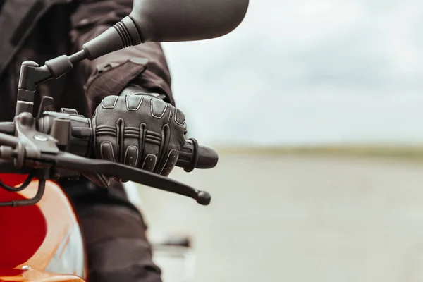 Motosikletli koruyucu eldivenli bir adam motosiklet tutuyor, yakın plan.
