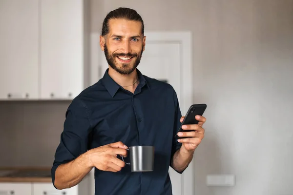 Чоловік Посміхається Тримає Мобільний Телефон Чашку Кави Або Чаю Дивлячись — стокове фото