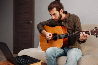 Evde akustik gitar çalmayı video öğreterek öğrenen konsantre bir adam
