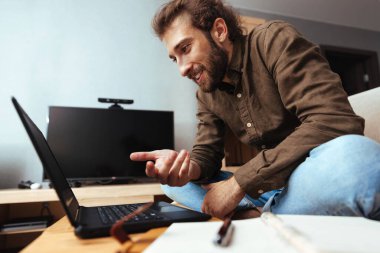 Evde, bilgisayarla konuşan sakallı genç adam.