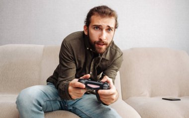 Bir adam video oyununda bir konsolda oyun kumandasını elinde tutarak hevesle oynuyor.