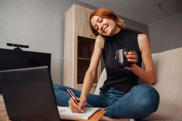 미소짓는 여자는 집에서 일하면서 핸드폰으로 이야기하고 노트북으로 있습니다 — 스톡 사진