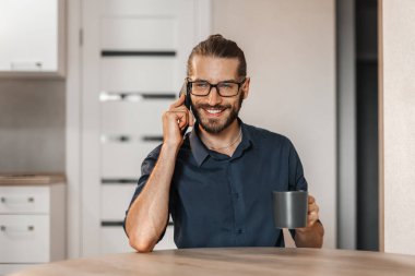 Dairesinde cep telefonuyla konuşan pozitif sakallı bir adam.