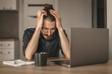 Başı ağrıyan üzgün bir adamın portresi iş yerinde dizüstü bilgisayarla oturmaktan yoruldu.