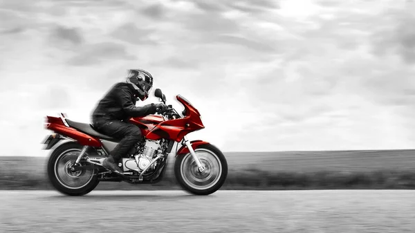 Bir motorcu yüksek hızda kırmızı bir motosiklet sürer. Siyah ve beyaz. Seçici renk efekti