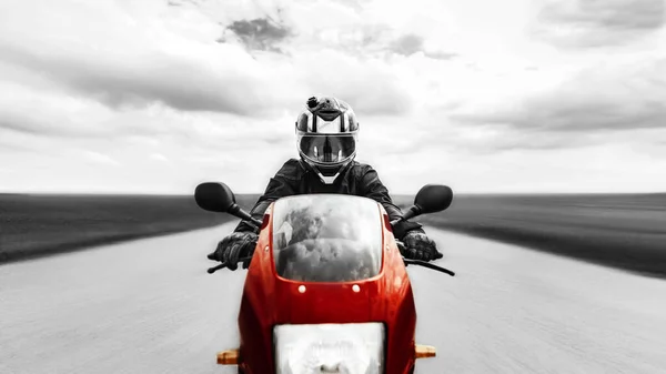 A man quickly rides on the road to the camera on a red motorcycle. Black and white photo