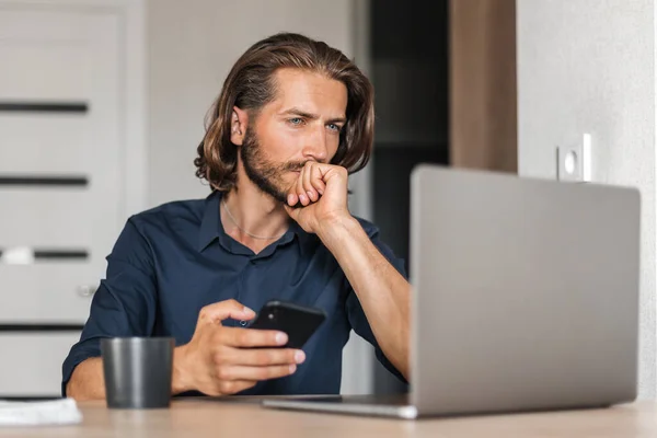 Hombre Concentrado Mirando Portátil Sosteniendo Teléfono Mano Punto Hacer Una — Foto de Stock