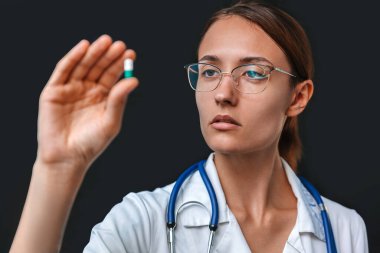 Genç bayan doktor kapsülde ilaçlara bakıyor. Gri arka planda izole edilmiş yakın plan fotoğraf.