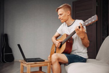 Konsantre olmuş genç adam online dersten gitar çalmayı öğreniyor.