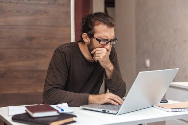 Dizüstü bilgisayarda çalışan sıkılmış bir hippinin portresi. Adam esneyip eliyle ağzını kapatıyor.