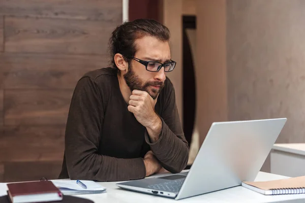 Hombre Serio Con Gafas Piensa Mientras Trabaja Ordenador Portátil Casa — Foto de Stock