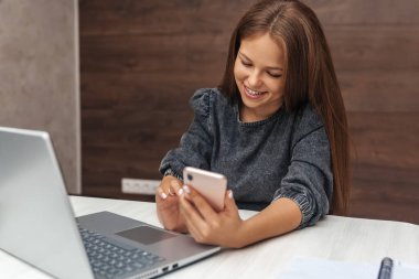 Gülümseyen genç kız masada otururken cep telefonuna mesaj yazıyor.