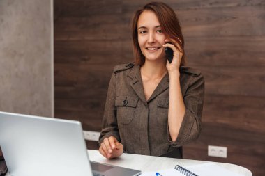 Güzel bir kadın cep telefonuyla konuşuyor ve gülümseyerek kameraya bakıyor. Evde çalışan kız.